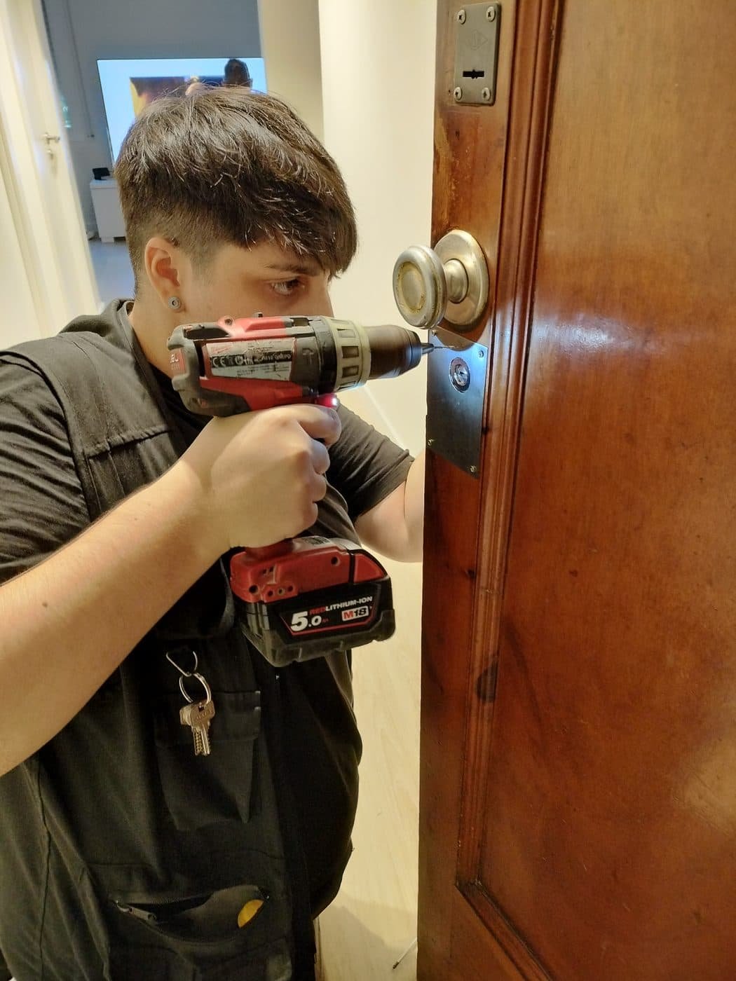 Profesional de Cerrajería BETA con un taladro instalando un escudo de seguridad en una puerta de madera