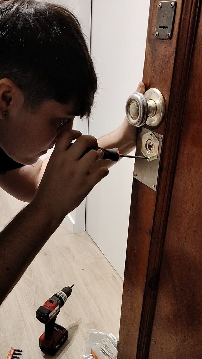 Profesional ajustando con un destornillador el bombín y el escudo de una puerta de madera