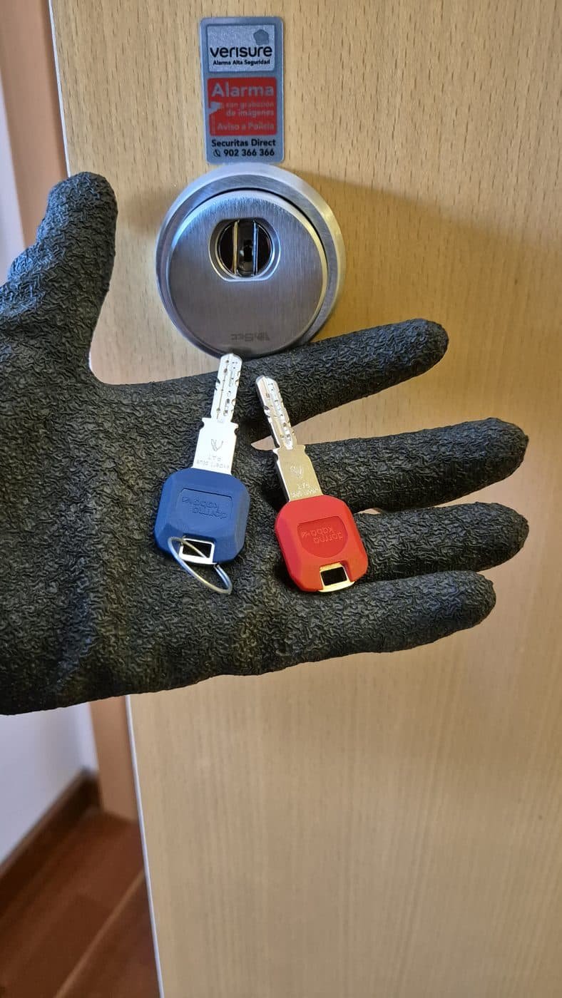 Bombín de seguridad recién instalado en una puerta y dos llaves nuevas sobre un guante de trabajo
