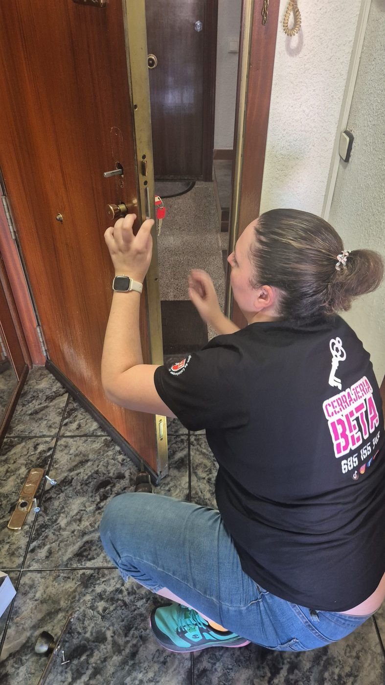 Profesional de Cerrajería BETA, de rodillas, trabajando en la cerradura de una puerta de madera